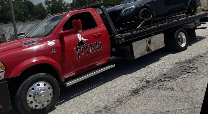 Titan red rollback flatbed with a car loaded on the deck.