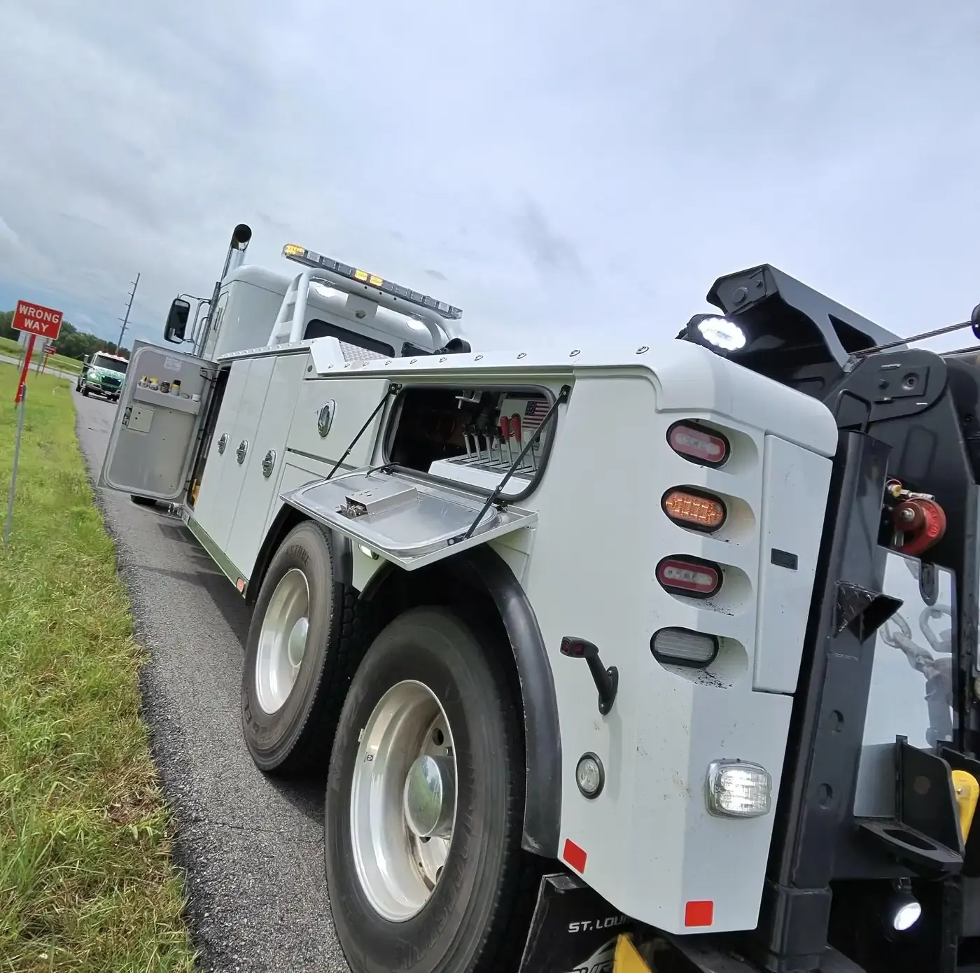 Titan heavy-duty wrecker parked on the shoulder with its boom out and the tool compartment open.
